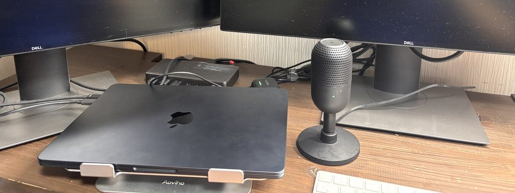 スタンドに置いて閉じたMacBookと外部モニター2台、外付けマイクのRazer Seiren V3 Miniを置いた作業机